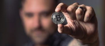 man holding up coin with bitcoin logo